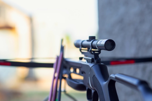 A modern crossbow with arrows and a telescopic sight lies on a wooden table in the street. Preparing for the hunt.