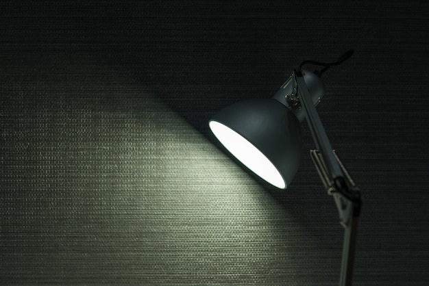 Современная настольная лампа освещается на фоне стены.