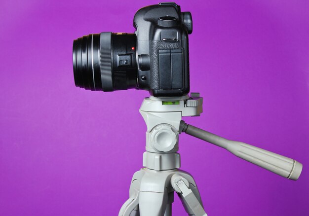 Modern digital camera with a tripod on purple table. Front view