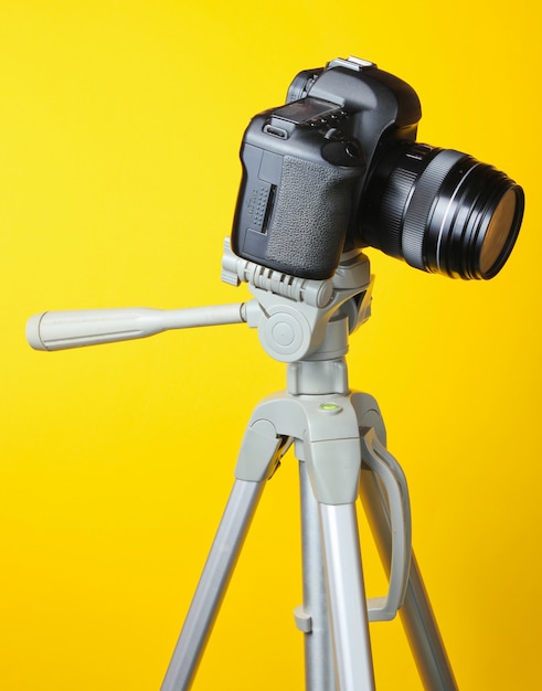 Modern digital camera with a tripod on a yellow table