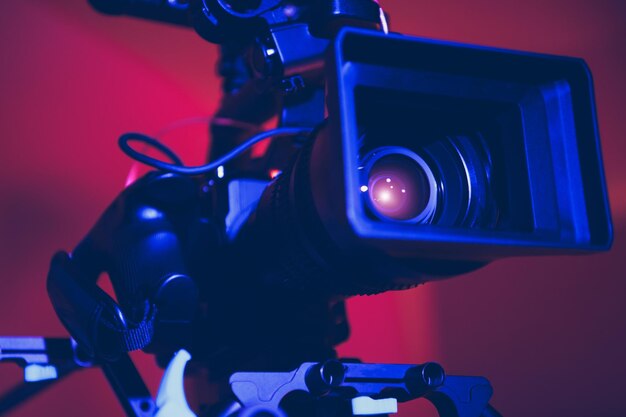 Modern Digital Cinema Camera with Moto Zoom Telephoto Lens Attached in Blue and Red Film Stage Illumination Close Up Film Industry Equipment