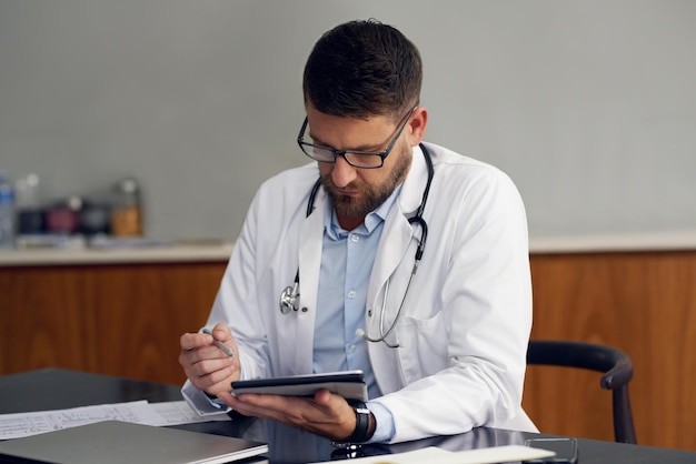 The modern doctor Cropped shot of a handsome male doctor working on his tablet while sitting in his office