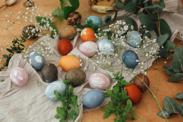 Photo modern easter eggs painted with natural dye on rustic background with flowers zero waste holiday stylish colorful easter eggs on wooden table with spring flowers and green branches