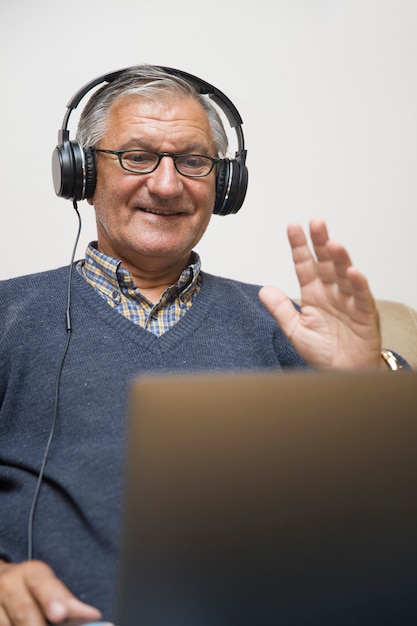 Modern elderly man siting at home with earphones and having online video call