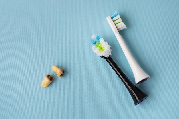 A modern electric toothbrush on a blue background next to extracted wisdom teeth affected by caries Tooth extraction operation Hygiene concept for daily care Old and new toothbrush