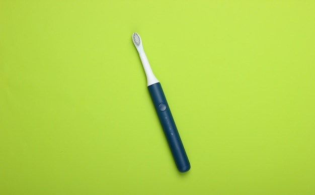 Modern electric toothbrush on green surface