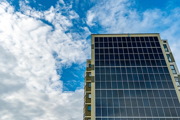 A modern energyefficient building against the background of clouds Multistorey residential building with solar panels on the wall Renewable energy sources in the city