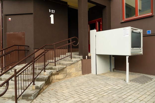 A modern entrance of a residential building equipped with a mechanism for lifting a wheelchair Lifting ramp with a mechanism for people with disabilities