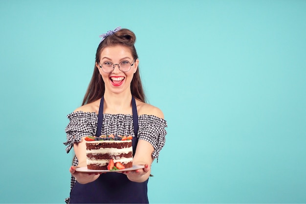 Il pasticcere femminile moderno sorride alla macchina fotografica con una torta in sue mani su una priorità bassa blu