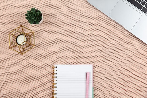 Modern female working space, top view. Laptop, cactus, candle, notebook on knitted blanket