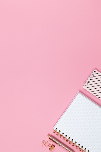 Modern female working space, top view. Notebooks, pen, clamp on pink background, copy space, flat lay.