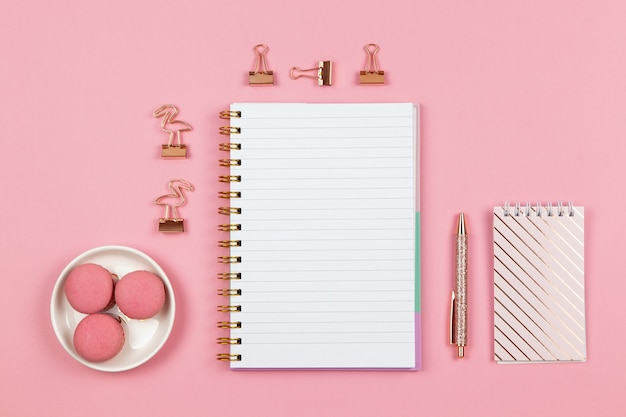 Modern female working space, top view. Notebooks, pen, clamps on pink background