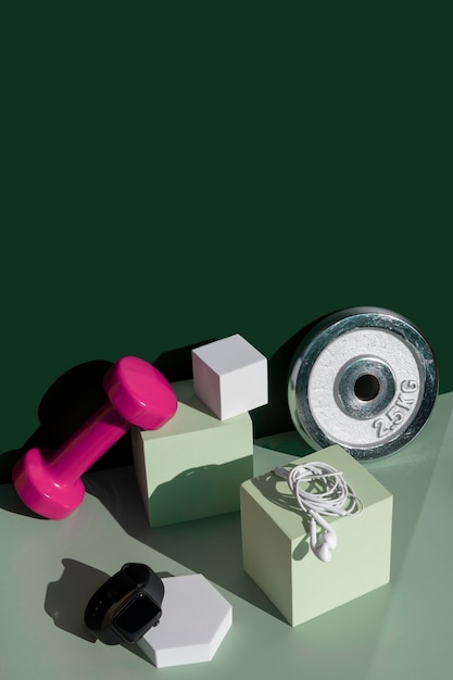 사진 컬러 블록 에메랄드 그린 및 민트 아이소메트릭 배경에 큐브 연단 무게, 이어폰 및 스마트 시계가 있는 현대적인 피트니스 구성