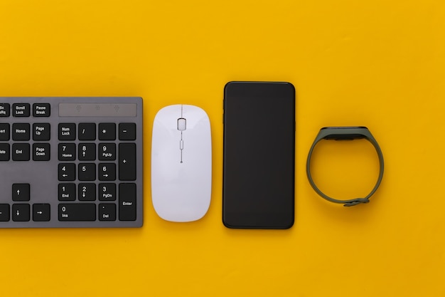 Modern gadgets. pc keyboard with pc mouse, smart bracelet and smartphone on yellow