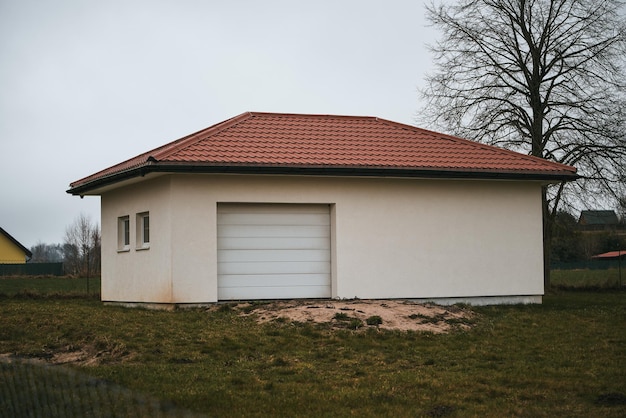 Modern garagegebouw met opgerolde witte muren en een rood pannendak en een autohangar met roldeur aan de buitenkant met witte poorten