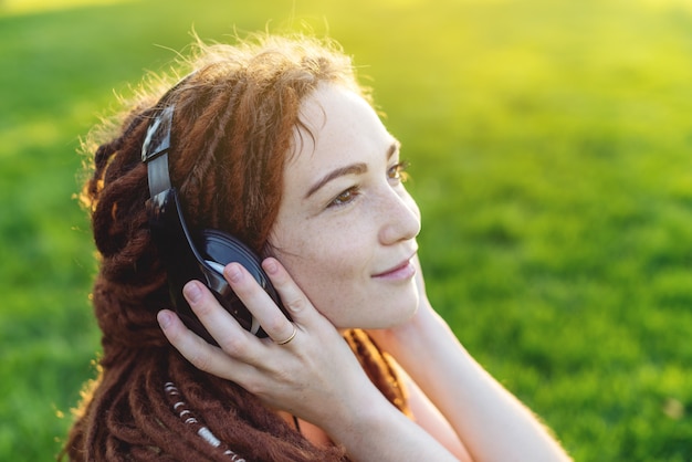 ドレッドヘアの秋の日当たりの良い公園で彼女のヘッドフォンで音楽を聴くと現代の女の子