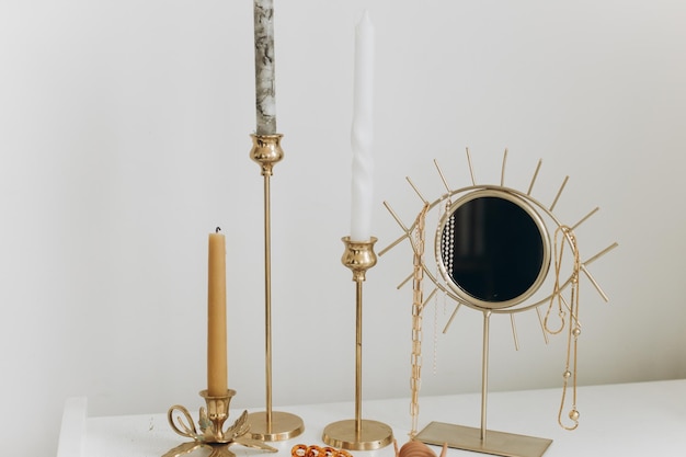 Photo modern gold boho mirror with gold necklace and vintage candles on white table jewellery and details