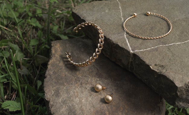 Bracciali e orecchini a forma di catena d'oro moderna e a forma di spirale su roccia all'aperto con spazio per le copie