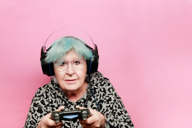 Modern grandmother with blue hair playing a video game with headphones and remote control has a camera