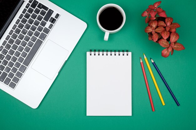 Modern green office desk table with laptop and blank notebook page for input the text