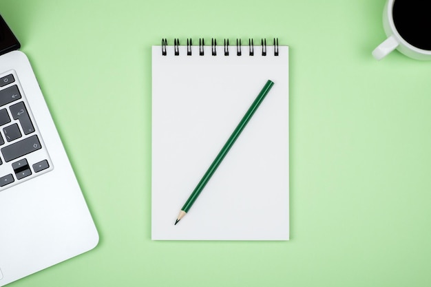 テキストを入力するためのラップトップと空白のノートブックページを備えた現代的な緑色のオフィスデスクテーブル