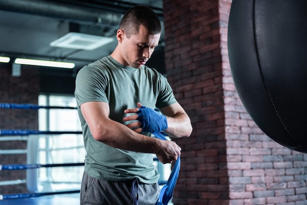 Modern gym. Dark-haired strong promising fighter standing in modern light gym while training hard