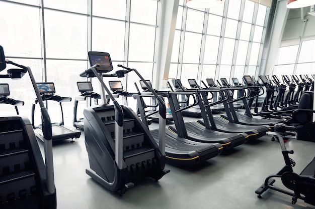 장비를 갖춘 현대적인 체육관 내부 저녁 역광에서 피트니스 심장 강화 훈련을 위한 런닝머신이 있는 피트니스 클럽 건강한 생활 방식 개념