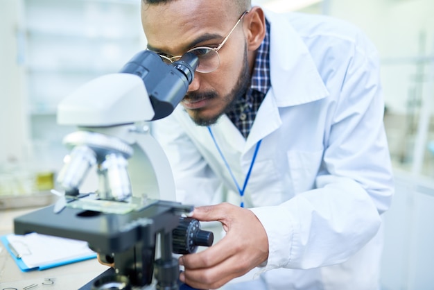 Modern handsome biologist adjusting microscope to zoom image