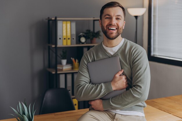 Photo modern happy bearded office male worker of it company smiling and holding laptop in office