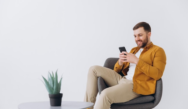 Modern happy millennial man using smartphone and typing on white background