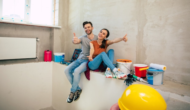 Modern happy young couple in love in casual clothes during new home repair or renovation of walls with a lot of tools for this