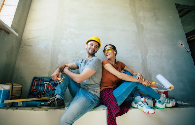 Современная счастливая молодая влюбленная пара в повседневной одежде во время ремонта нового дома или ремонта стен с большим количеством инструментов для этого