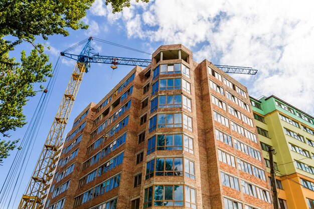 Modern high storey building under construction with tower crane and green tree