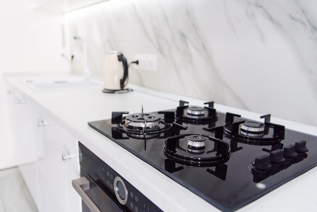 Photo modern high-tech black gas stove with sensor panel in the bright interior of the kitchen with white marble tiles.