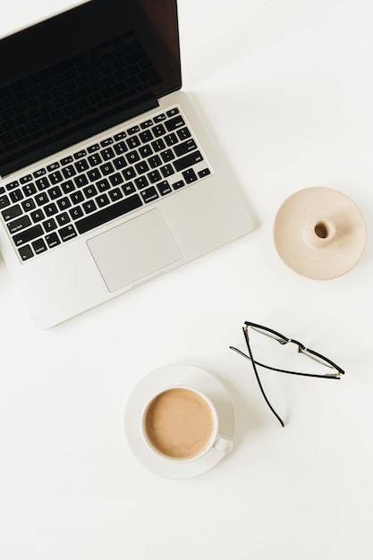 Modern home office desk workspace with laptop, cup of coffee, glasses on white surface