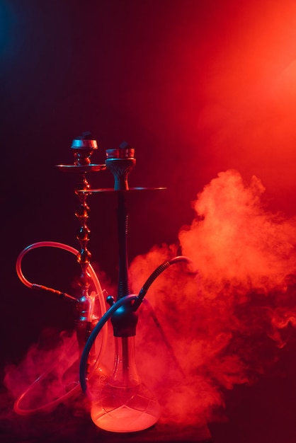 Modern hookah, shisha on a smoky black background with colored lighting and smoke