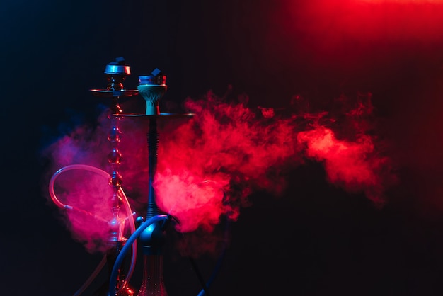 Modern hookah, shisha on a smoky black background with neon lighting and smoke. Place for your text