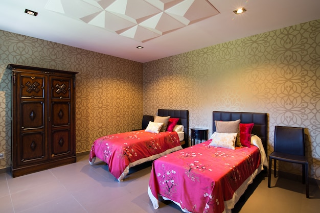 Modern house room, with wallpaper and two single beds with\
fuchsia duvets. decorative ceiling.