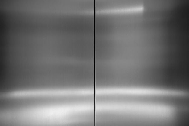 現代の産業メタリックな背景。表面に反射した光沢のある明るい光でエレベータードアステンレス鋼表面のテクスチャの写真を閉じる