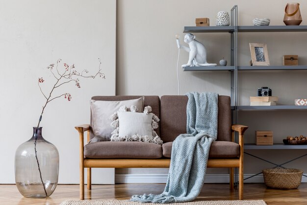 Modern interieur van woonkamer met bruine houten bank, grijze boekenstandaard, glazige vaas met bloemen en elegante accessoires. Beige en japandi-concept. Stijlvolle huisstaging. Ruimte kopiëren.