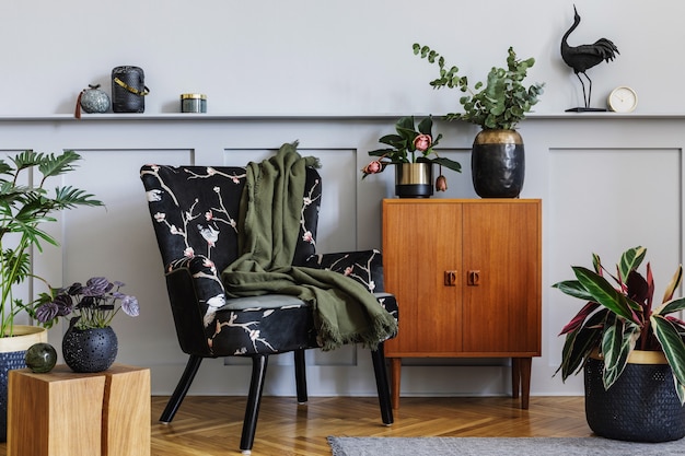 Modern interieur van woonkamer met design fauteuil, houten vintage commode, houten lambrisering met plank, planten, kubus, tapijt, grijze muur, decoratie en persoonlijke accessoires in home decor.