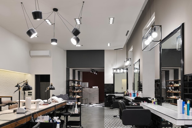 Modern interior of the beauty salon which consist of nail salon and barbershop with black lamps and concrete wall Mirrors chairs backwashes and other equipment are in the salon