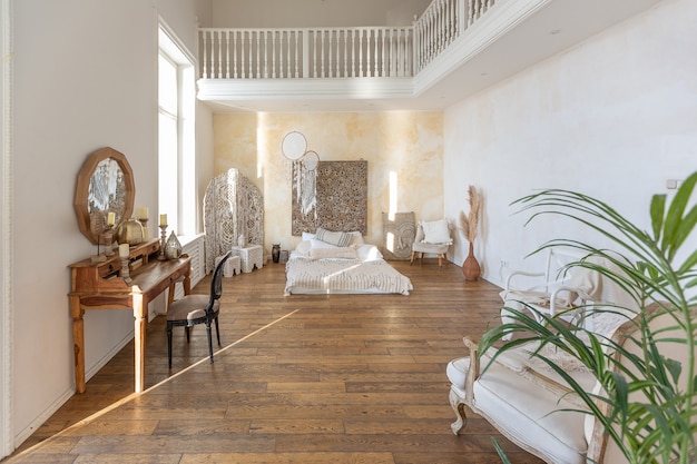 modern interior of a bright room in a two-storey apartment with decorative items in bali style with a balcony. white walls, wood floors and vintage furniture