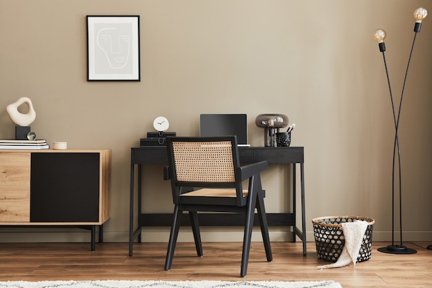 세련된 의자, 책상, 옷장, 검은색 모의 포스터 프레임, 라파톱, 책, 사무용품 및 가정 장식의 우아한 개인용 액세서리를 갖춘 홈 오피스 공간의 현대적인 인테리어 디자인