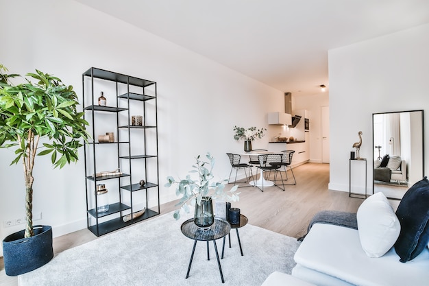 Photo modern interior design of lounge zone with light gray soft furniture with cushions and decorative tables placed on carpet in spacious apartment with white walls