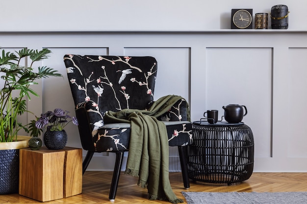 Modern interior of living room with design armchair, wood paneling with shelf, plants, coffee table, grey wall, decoration, carpet, copy space and persnoal accessories in stylish home decor.