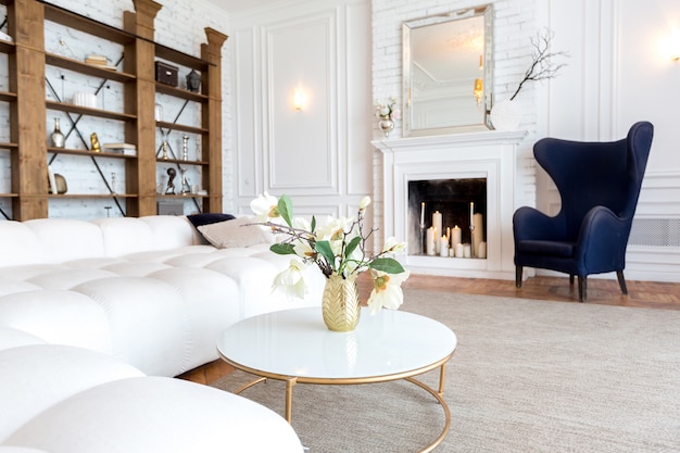 Modern interior of a luxurious large bright living room. white expensive sofa and wooden shelving, white walls with moldings and a luxurious chandelier