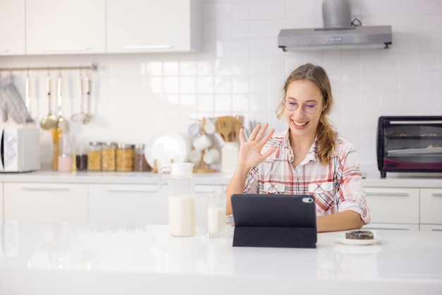 In a modern kitchen, a gorgeous young woman uses a digital tablet while eating a healthy breakfast.