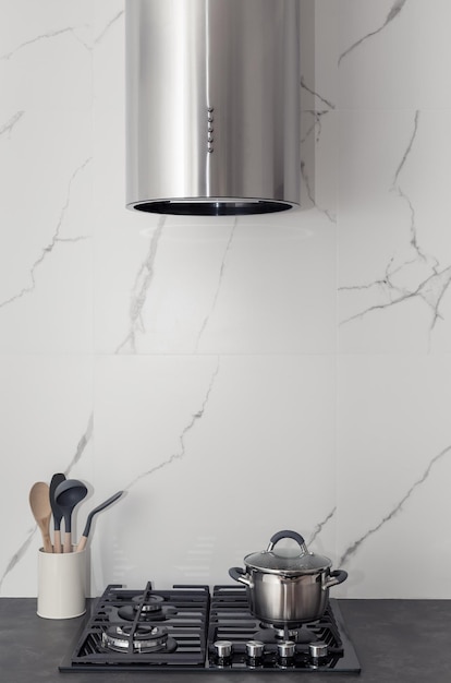 Современный интерьер кухни с серебряной кухонной вытяжкой на газовой плите и плиточным мраморным фартуком