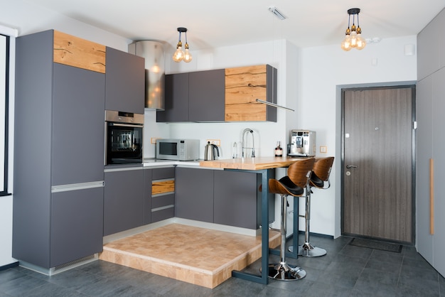 Modern kitchen interior with lights on Brown wooden table and bar stools, coffee machine. Contemporary interior with loft elements